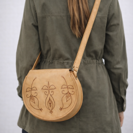 Mujer llevando bolso redondo artesanal de cuero natural con diseño floral grabado a mano y correa ajustable.