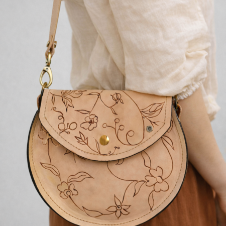 Mujer llevando un bolso redondo artesanal de cuero natural Pajarico con grabado floral realizado a mano.