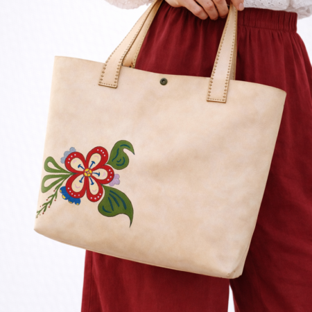 Mujer sosteniendo bolso tote artesanal de cuero natural con flor tradicional pintada a mano en colores rojo, verde y azul.