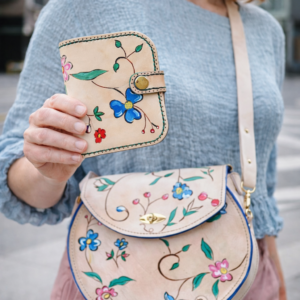 Mujer sosteniendo un monedero artesanal de cuero natural con diseño floral pintado a mano a juego con un bolso de piel artesanal.