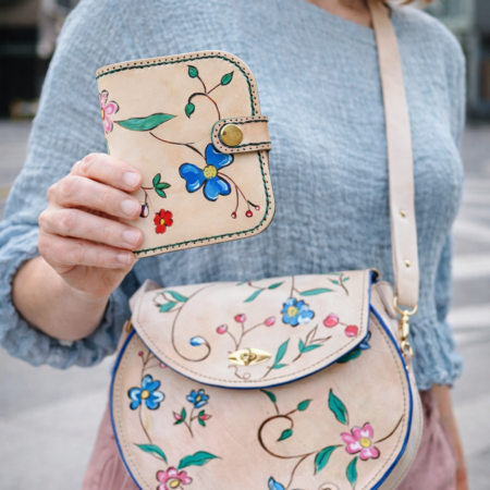 Mujer sosteniendo un monedero artesanal de cuero natural con diseño floral pintado a mano a juego con un bolso de piel artesanal.