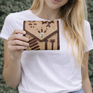 Mujer sosteniendo un monedero artesanal de cuero con cierre tipo sobre y diseño tribal pintado a mano.