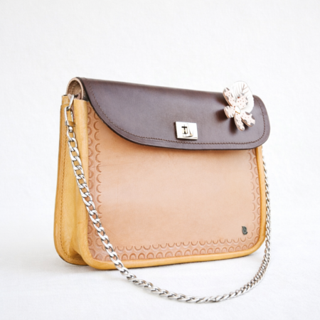 Bolso bandolera artesanal de cuero bicolor con solapa marrón y detalle floral decorativo, visto de frente.