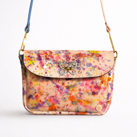 Bolso bandolera artesanal de cuero con diseño de salpicaduras multicolor pintadas a mano y cierre decorativo en forma de mariposa.