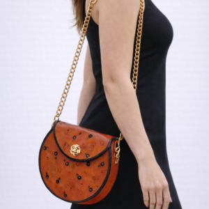 Mujer llevando un bolso redondo artesanal de cuero color cuero tostado Pajarico con cadena metálica dorada.