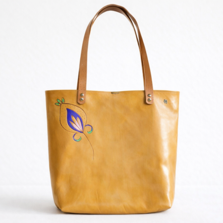 Bolso tote artesanal de cuero natural con motivo floral violeta pintado a mano en la parte frontal.