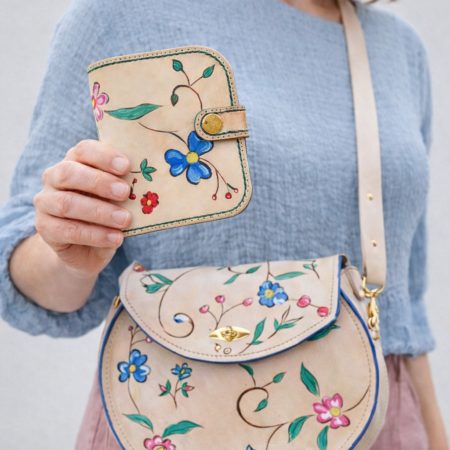 Mujer llevando un bolso redondo artesanal de cuero Pajarico con flores de colores pintadas a mano sobre cuero natural.