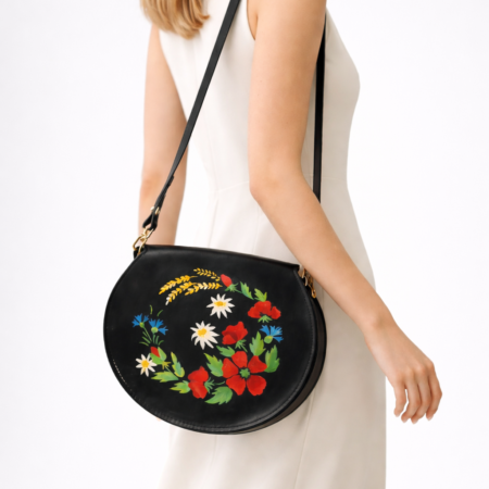 Mujer llevando un bolso redondo artesanal de cuero negro Pajarico con diseño floral pintado a mano.