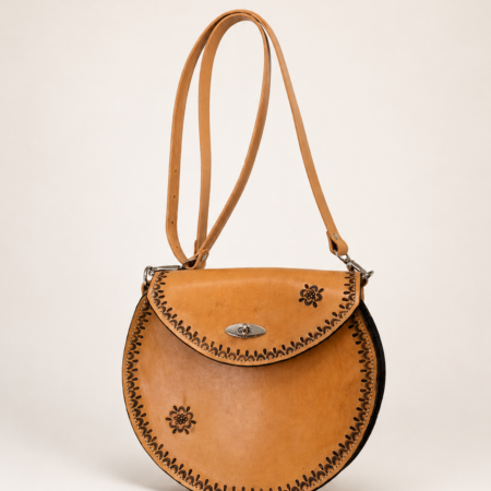 Bolso redondo artesanal de cuero natural Pajarico con detalles florales grabados y cierre metálico frontal.