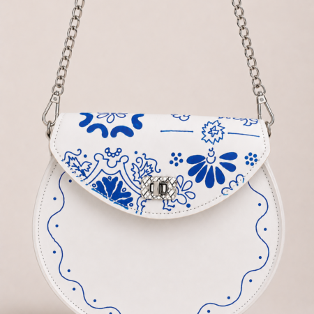 Bolso redondo artesanal de cuero blanco con decoración azul inspirada en la cerámica tradicional, visto de frente.