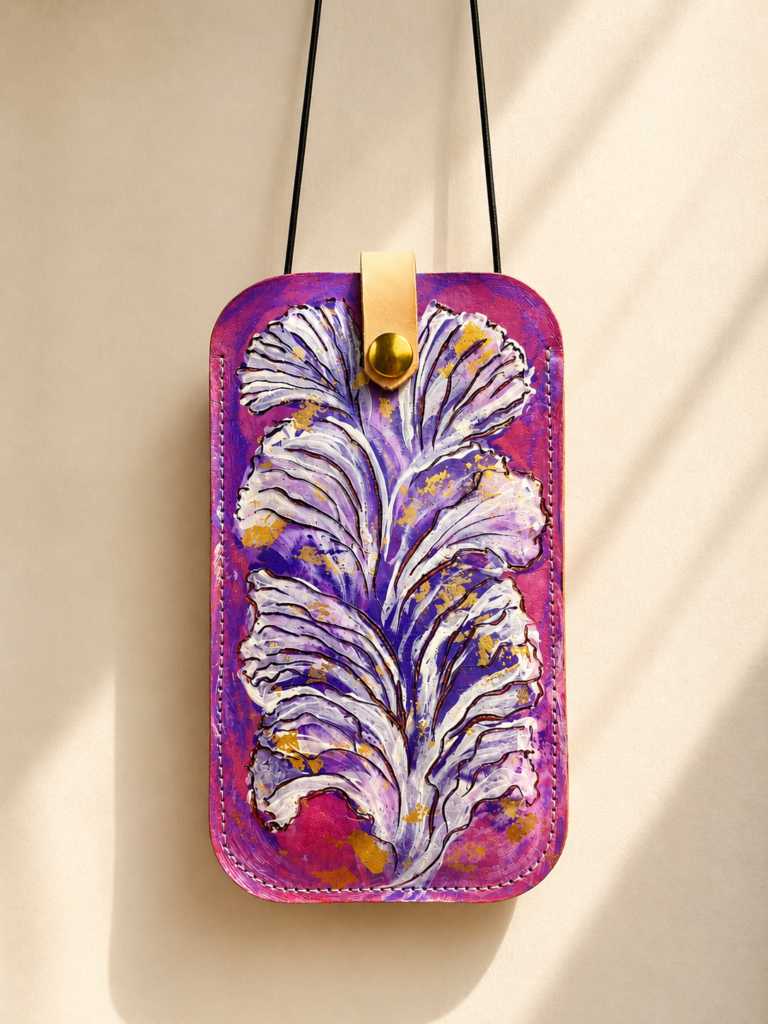 Porta móvil artesanal de cuero Pajarico con diseño de pluma violeta pintada a mano sobre fondo fucsia.